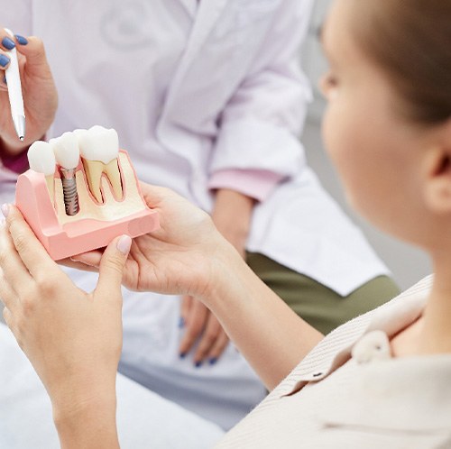 Dentist pointing to large model dental implant held by patient