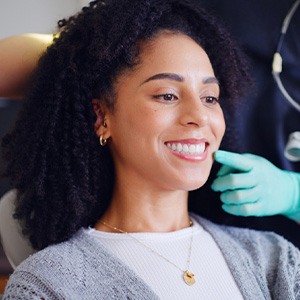 Dentist with green gloves pointing to woman’s smile