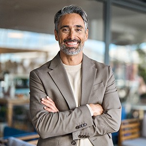 Man in taupe suit with gray in his hair smiling with glass windows behind him