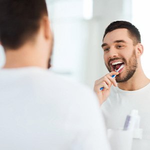 Man smiling while brushing his teeth