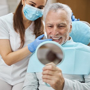 Dentist touching teeth of man with white hair looking at smile in handheld mirror