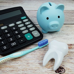 Calculator, piggy bank, toothbrush, and model tooth on wooden surface